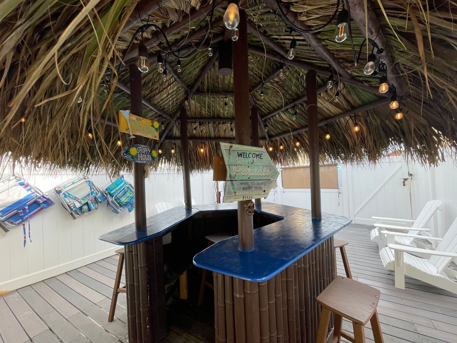 The private thatched-roof tiki bar with string lights and bar stools on the fenced back deck